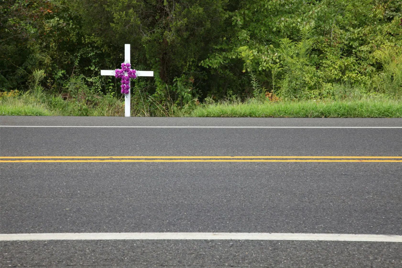 Blog 1 A white cross with roses on it alongside a road