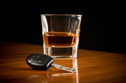 Man Admits to Driving Drunk During Crash That Killed 5 1 Glass of dark liquor on a table next to a car key.