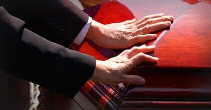 Man, Infant Killed in Alabama Trucking Accident 1 Two people with their hands placed on a casket at a funeral.