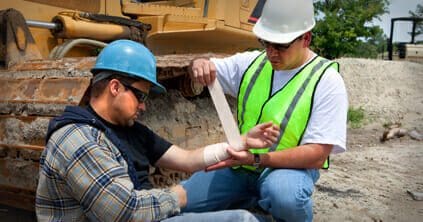 One construction worker bandaging another's forearm